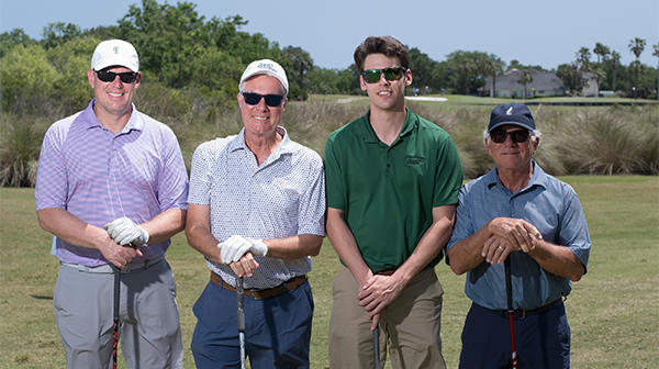 Four golfers smiling holding golf clubs